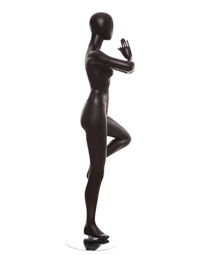 A glossy black female mannequin statue in a yoga tree pose, standing on a small round base against a plain white background.