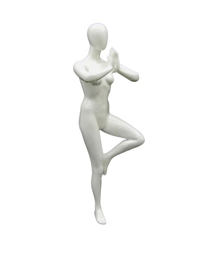 Posable female yoga mannequin in white practicing tree pose, showcasing flexibility and balance for display or photography.